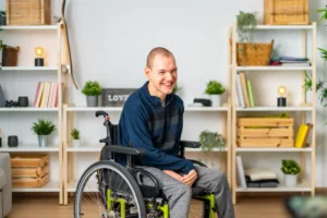 Smiling man in a wheelchair in a bright, homey room with shelves and plants