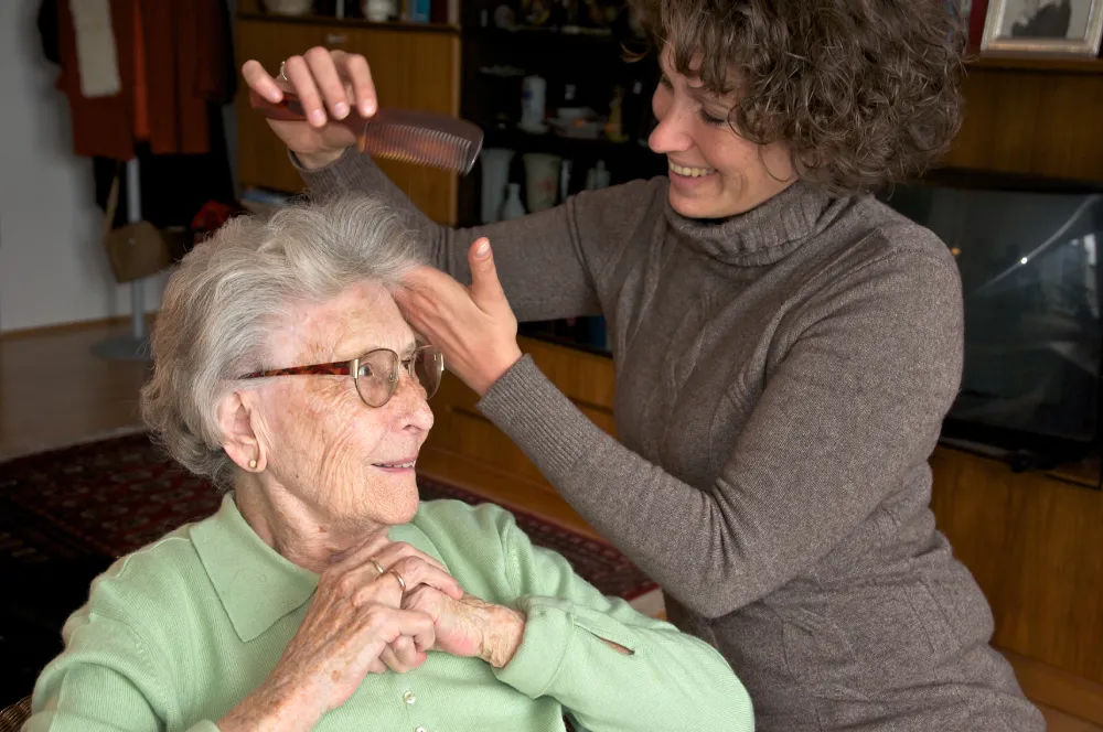 Care worker smiling while gently combing elderly woman’s hair at home